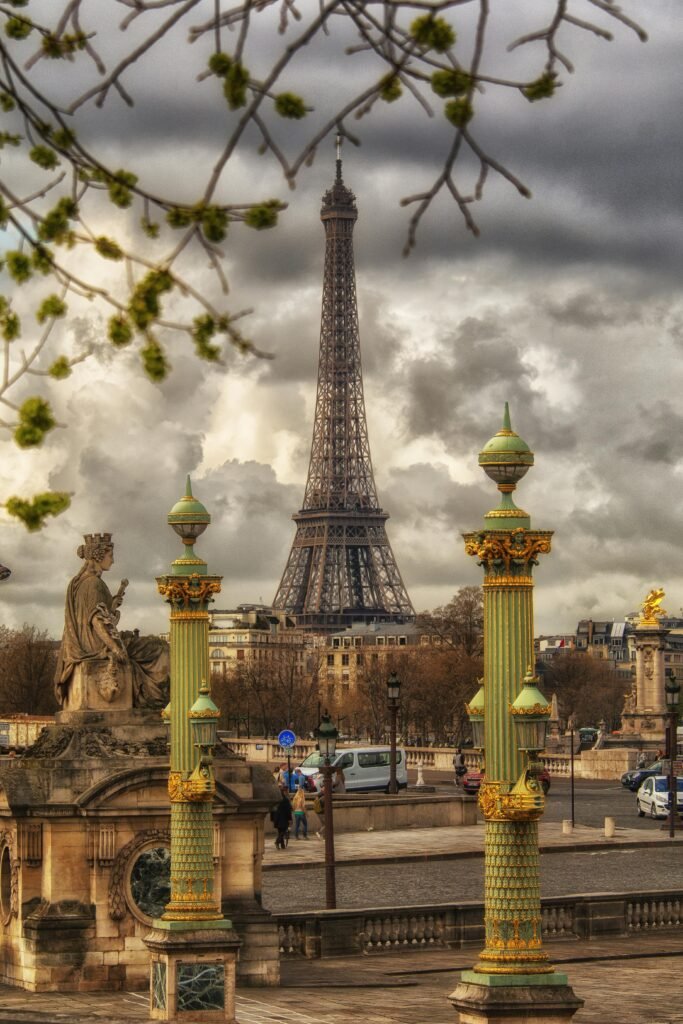 A captivating view of the Eiffel Tower framed by historic sculptures and columns in Paris under a cloudy sky.