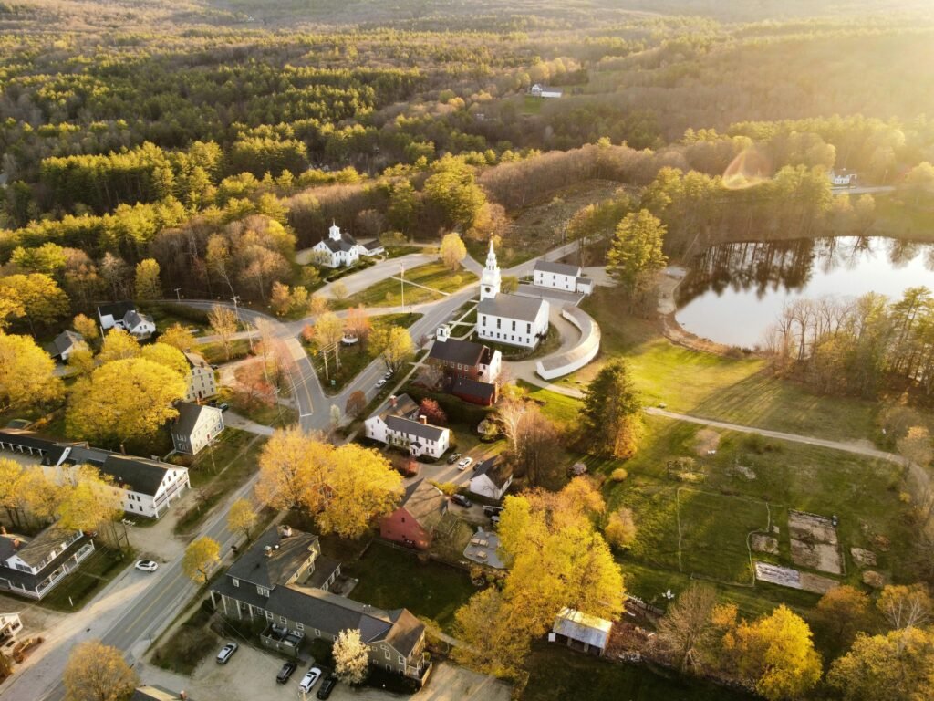 Aerial view of Hancock, NH showcasing fall foliage, a church, and a tranquil lake.