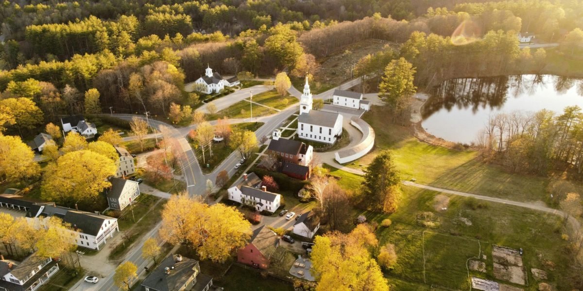 Aerial view of Hancock, NH showcasing fall foliage, a church, and a tranquil lake.