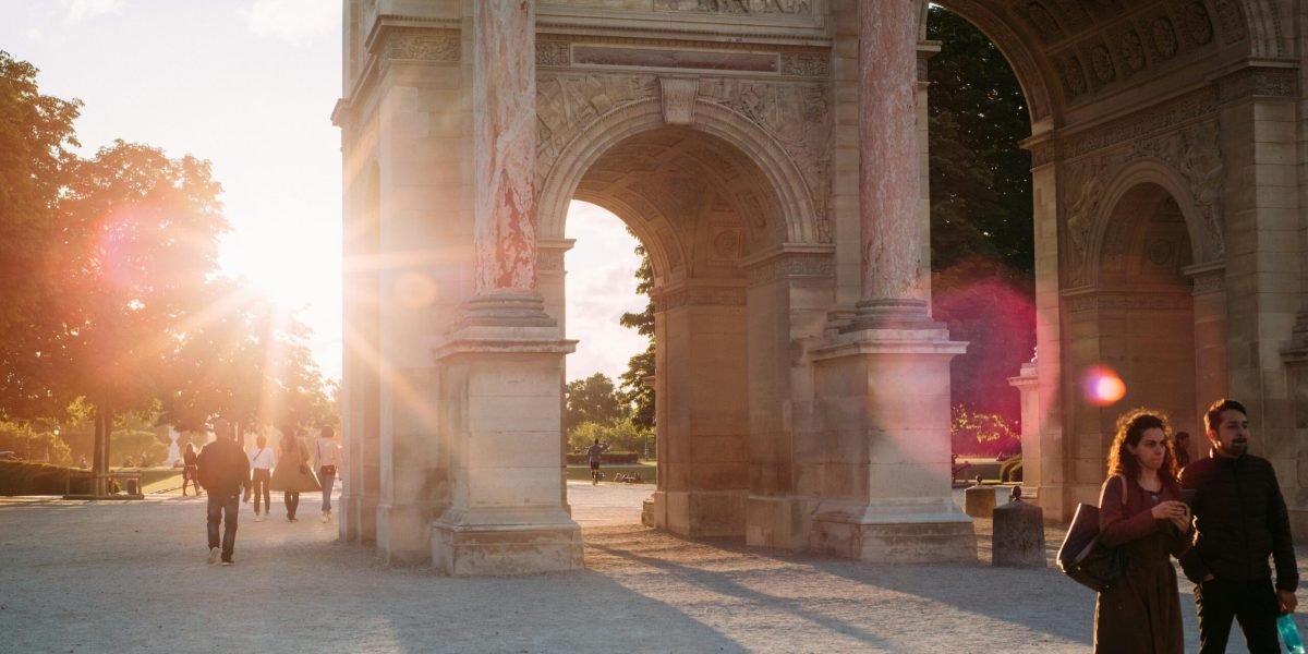 A romantic scene with sunrays shining through a Parisian archway, featuring people strolling.