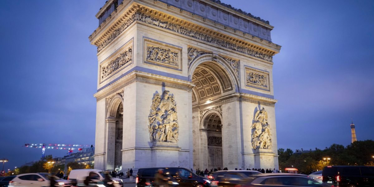 Iconic Arc de Triomphe under blue evening sky with bustling traffic in Paris.