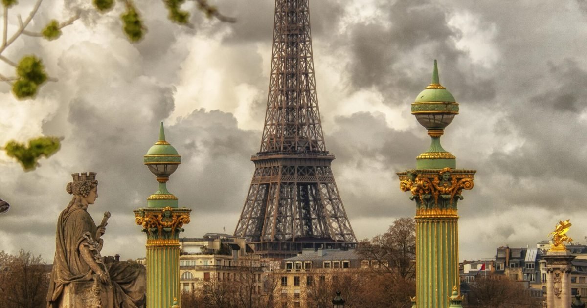 A captivating view of the Eiffel Tower framed by historic sculptures and columns in Paris under a cloudy sky.